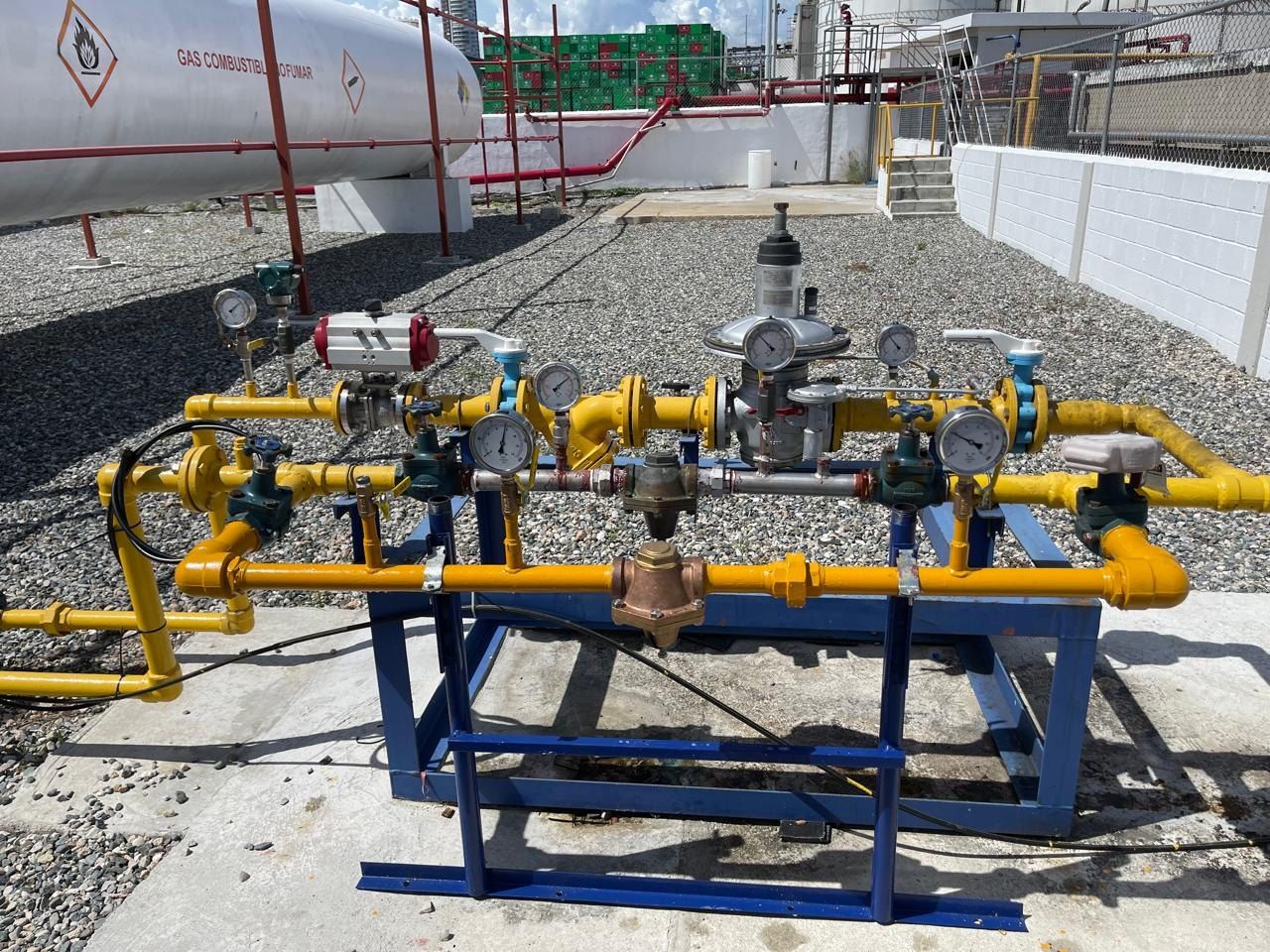 Estación de regulación de gas con tuberías amarillas, reguladores y manómetros junto a tanques de GLP